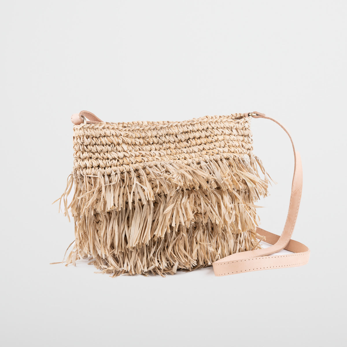 Small light raffia handbag with fringing detail. Fully lined with inside pocket, adjustable leather shoulder straps and magnetic clasp closing. 