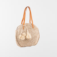 Round raffia handbag with pom-pom decoration and adjustable leather shoulder straps. Fully lined with inside pocket. Available in beige.